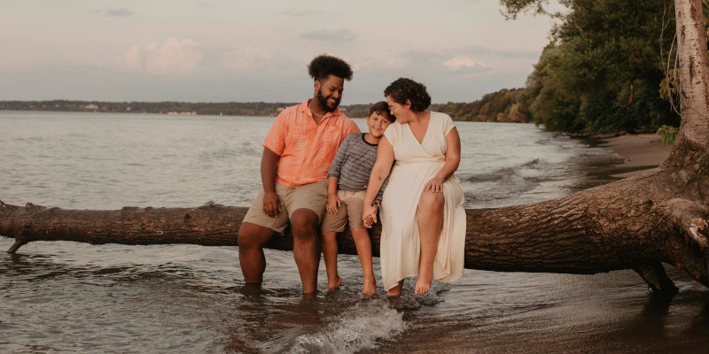 Life insurance - Couple and their son sitting on a tree branch over a lake.